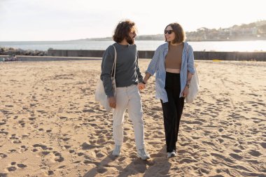 Aşık mutlu çift güneşli sahilde el ele yürür. Yüksek kalite fotoğraf