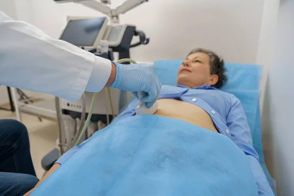 Middle aged woman patient lying on bed and having ultrasound examination of abdomen in clinic