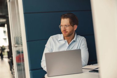 Laptop üzerinde çalışan yakışıklı girişimci iş günü boyunca modern iş yerinde oturuyor.