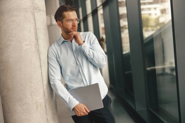 Ofis arka planında dizüstü bilgisayarı olan gözlüklü şık bir işadamı. 