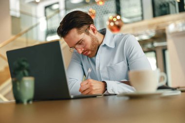 Laptop kullanırken proje üzerinde çalışan yakışıklı iş adamı ve ofiste otururken notlar alıyor.