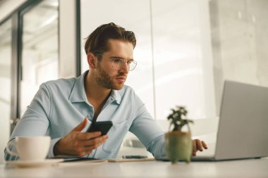 Modern ofiste dizüstü bilgisayarla çalışırken elinde telefon tutan erkek girişimci. Yüksek kalite fotoğraf