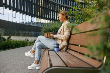 İş kadını kahve içiyor ve ofis dışında dizüstü bilgisayarla çalışıyor. Mesafe çalışma kavramı
