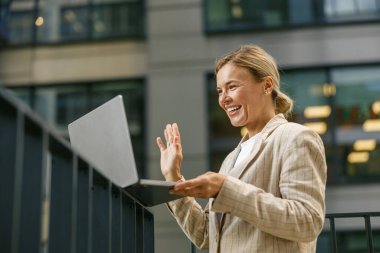 Ofis dışında video konferansı yapılırken gülümseyen bayan yöneticinin meslektaşlarına el sallaması.
