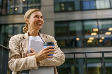 Satış müdürü, teneffüste dizüstü bilgisayar ve kahveyle ofisin terasında duruyor ve yüzünü çeviriyor.