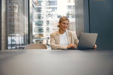 Dizüstü bilgisayarda çalışan şık bir iş kadını ofis arka planında oturuyor. 