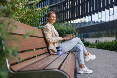 Kadın yönetici kahve içiyor ve ofis dışında dizüstü bilgisayarla çalışıyor. Mesafe çalışma kavramı