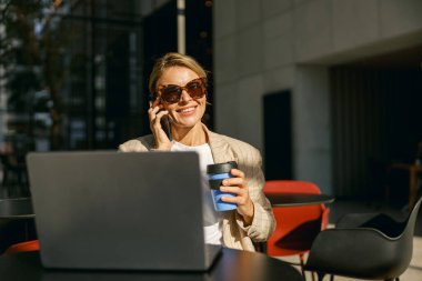 Modern bir iş arkadaşı olan kadın bilgisayarla çalışırken müşteriyle telefonda konuşuyor. 