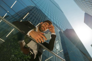 Gökdelenlerin arka planında duran cep telefonu kullanan yakışıklı girişimcinin alt görünümü