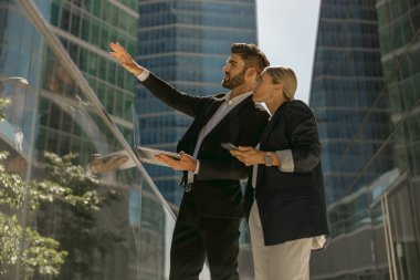 İş adamı ofis terasında dururken bayan meslektaşına bir şey gösteriyor.