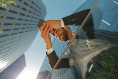 Gökdelenlerin arka planında duran cep telefonu kullanan yakışıklı girişimcinin alt görünümü