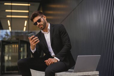 Cep telefonlu bir işadamı ofis binasının arka planında bankta oturuyor. Yüksek kalite fotoğraf