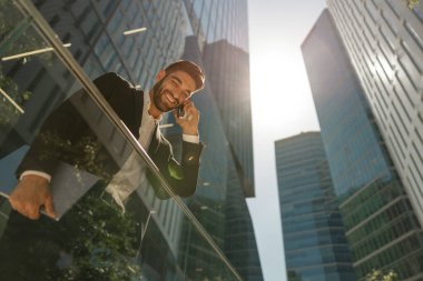 Gökdelenlerin arka planında duran, cep telefonuyla konuşan yakışıklı iş adamının alt görüntüsü.