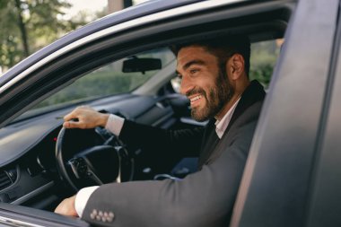 Takım elbiseli erkek sürücü direksiyonun başına geçiyor ve başını çeviriyor. Yüksek kalite fotoğraf