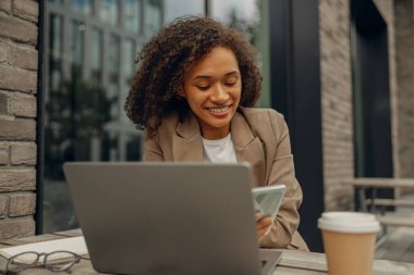 Kafe terasında otururken dizüstü bilgisayarda çalışan gülümseyen serbest çalışan kadın. Mesafe çalışma kavramı
