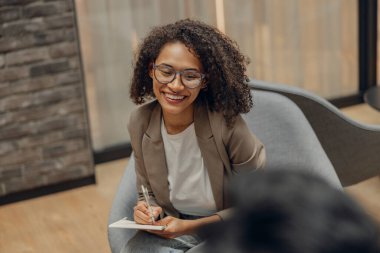 Gülümseyen bayan yönetici, iş arkadaşlarıyla iş yerinde yaptığı toplantıda notlar alıyor.