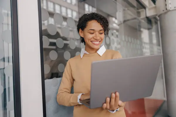 stock image Smiling female manager using laptop while standing on modern office background 