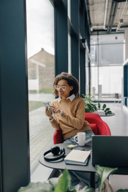 Gülümseyen kadın yönetici, tatilde ofiste otururken cep telefonu kullanıyor.
