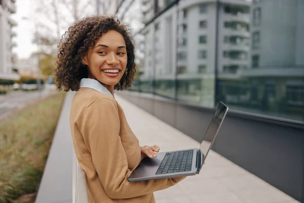 Happy business woman working laptop while standing outside on background of office building