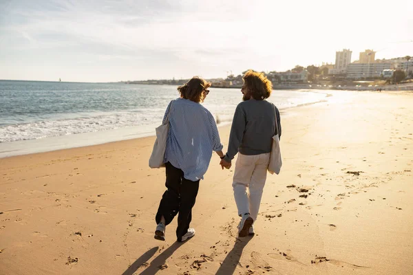 Birbirine aşık çiftlerin arka görüntüsü güneşli sahilde el ele yürümektir. Yüksek kalite fotoğraf