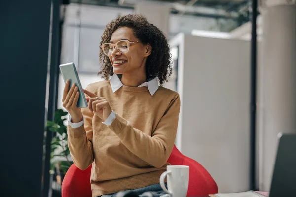Smiling woman executive manager is using mobile phone sitting in office during break time