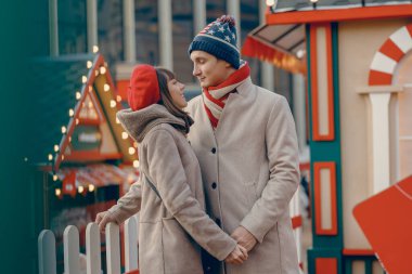 Tatil ışıklarıyla çevrili, kışlık şapkalı bir çift, Noel fuarına sevgi dolu bir bakışla romantizm buluyor.