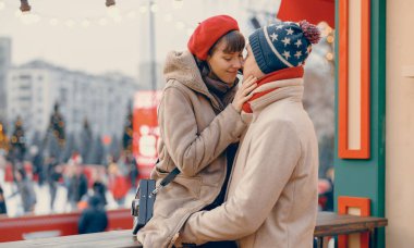 Bir kadın eşinin yüzüne nazikçe dokunur, Noel pazarında yakın bir anı paylaşır ve arka planda ışıldayan ışıklar olur..