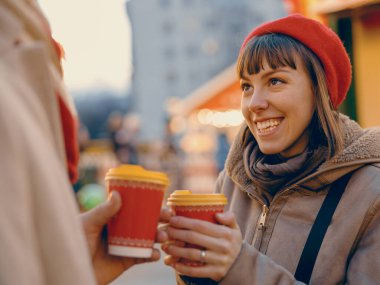 Genç bir kadın, elinde mevsimlik bir içki tutarak ortağına ışıldıyor. Paylaştıkları mutluluk, Noel Fuarı 'ndaki şenlikli içecekler kadar sıcak.