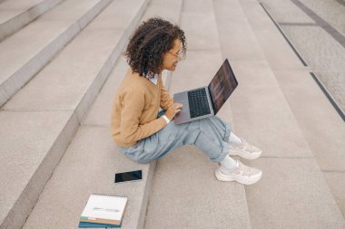 Serbest çalışan bir kadın, meslektaşı merdivenlerde otururken görüntülü görüşme yapıyor.