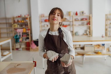 Güzel bir kadın çömlek atölyesindeki ahşap bir masada kupa yapmak için kil hazırlıyor.