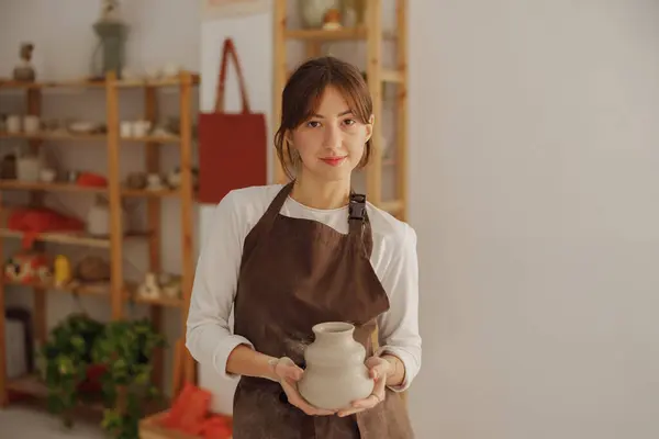 Confident entrepreneur crafts woman holding mug in pottery studio while looking at camera