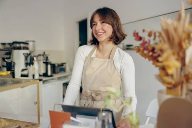 Kahve dükkanında tezgahın arkasında duran mutlu bir bayan baristanın portresi.