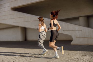 Spor giyimli iki atletik kadın sabahın erken saatlerinde şehirde koşuyor. Hedefe ulaşılıyor.