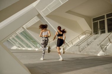 Spor giyimli iki atletik kadın sabahın erken saatlerinde şehirde koşuyor. Hedefe ulaşılıyor.