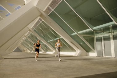 Spor giyimli iki atletik kadın sabahın erken saatlerinde şehirde koşuyor. Hedefe ulaşılıyor.