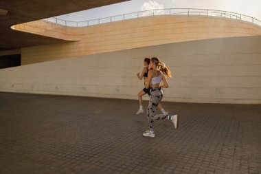 Spor giyim sektöründe iki genç kadın modern binalarda koşuyor. Etkin yaşam tarzı kavramı