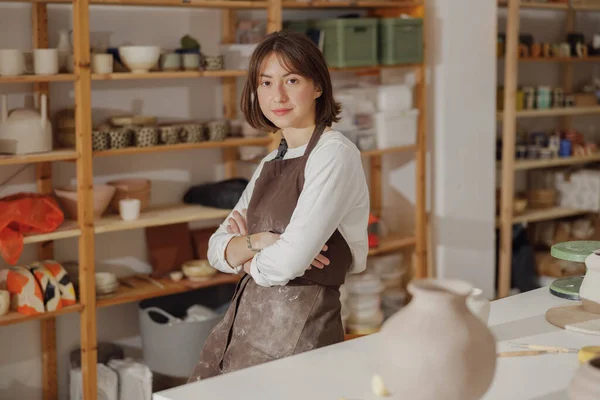 Smiling entrepreneur crafts woman in pottery studio while looking at camera