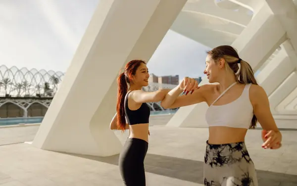 Sporty happy female friends doing elbow greeting before starting morning workout outside