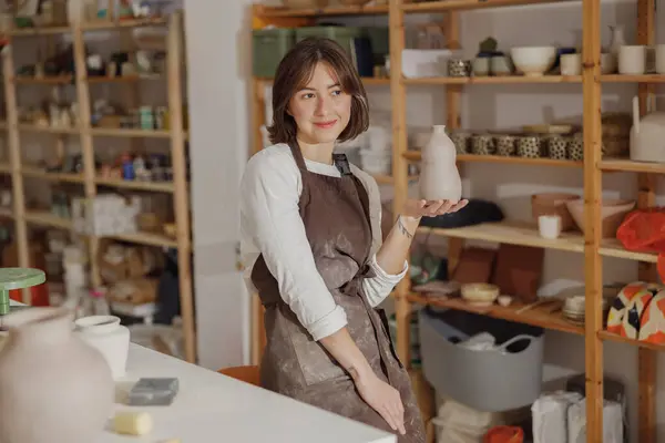 Smiling entrepreneur crafts woman holding mug in pottery studio while looks away