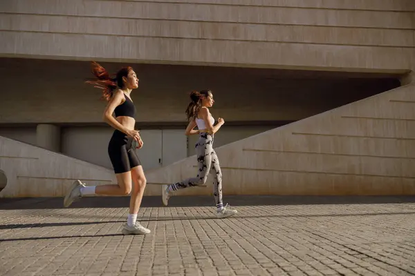 Spor giyim sektöründe iki genç kadın modern binalarda koşuyor. Etkin yaşam tarzı kavramı