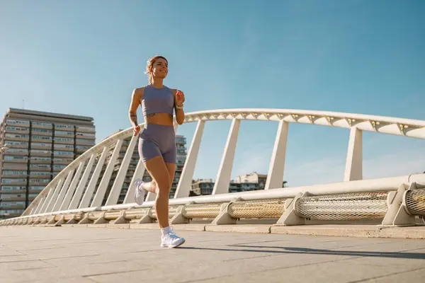Active woman athlete running on bridge along an outdoor track on modern buildings background