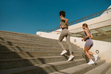 Güneşli bir günde dışarıda koşan spor giyimli iki aktif bayan sporcu arkadaş.