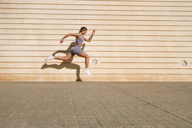 Spor kıyafetli genç bir kadın arka planda duvarla havaya sıçrıyor. Yüksek kalite fotoğraf