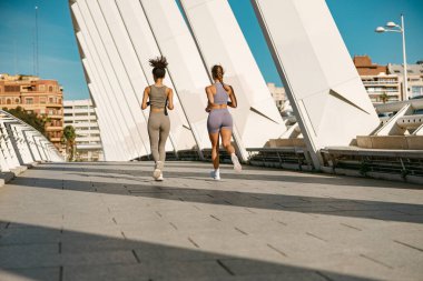 Spor giyim sektöründe iki genç kadın modern binalarda koşuyor. Etkin yaşam tarzı kavramı