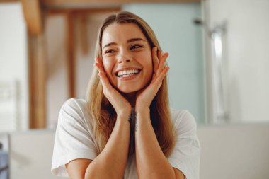 Çekici bir kadın güzel yüzüne dokunuyor ve banyoda dururken gülümsüyor.