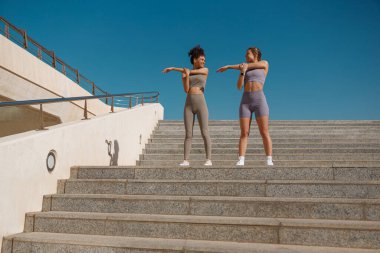 Eşofmanlı genç sporcu kadınlar dışarıda esniyorlar ve koşuya hazırlanıyorlar. Sağlıklı yaşam konsepti