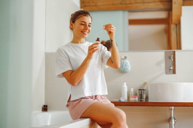 Yüzüne serum süren çekici bir kadın. Nemlendirici ve cilt bakımı. Banyoda duruyor.