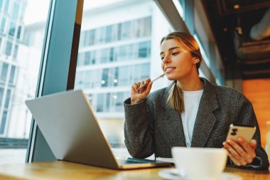 Rahat bir kafede otururken dizüstü bilgisayarda çalışan şık, genç bir bayan serbest yazar. 