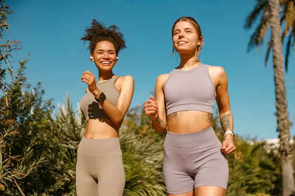 Two active women athlete running side by side along an outdoor track on public park background