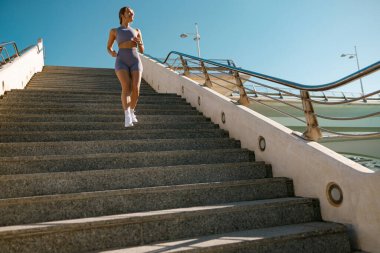 Spor giyimli atletik kadın sabahın erken saatlerinde şehirde koşuyor. Hedefe ulaşılıyor.